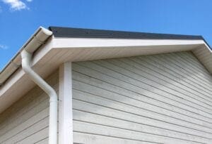 Close-up of a house corner with gray siding and white trim under a clear blue sky.